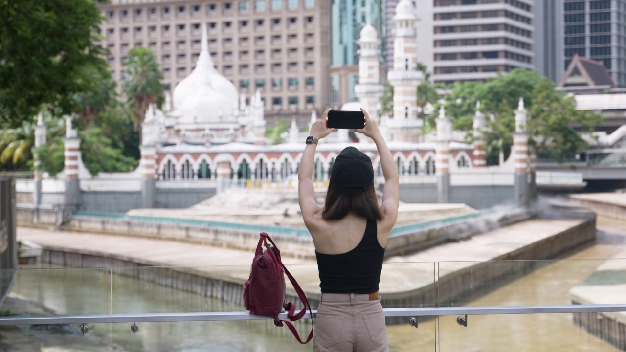 一名亚洲女子在吉隆坡的Masjid Jamek瞭望点旅行时用智能手机拍照视频下载