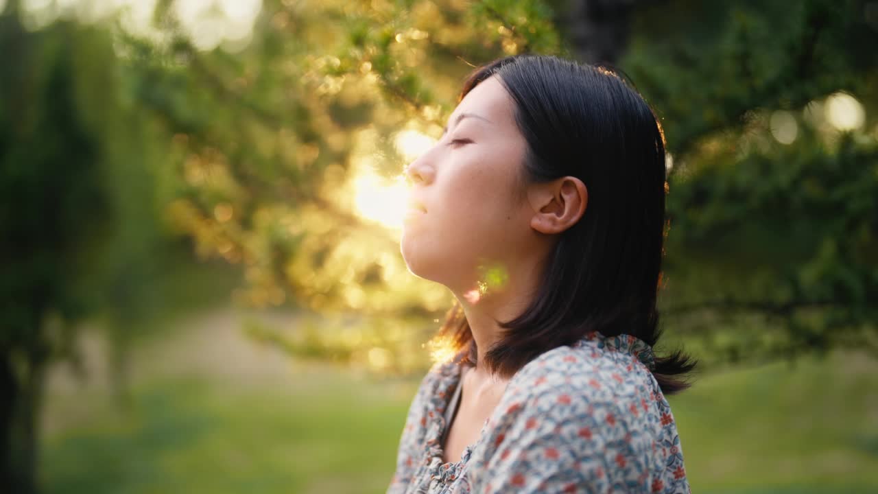 年轻女子的肖像与她的眼睛闭在自然在日落视频素材