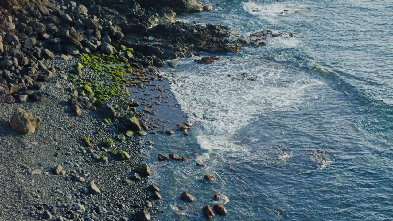 日落时，海浪冲击着火山流线型的石头。黑色的岩石海滩，平静的海洋，海浪形成泡沫。视频素材