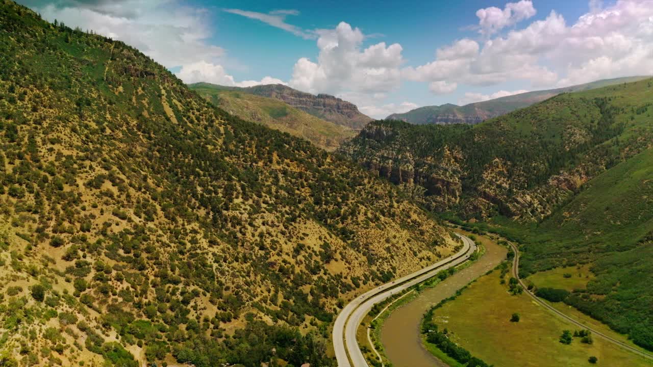 汽车沿着环绕绿色山丘的道路行驶。晴朗如画的山在多云的蓝天的背景下。视频素材