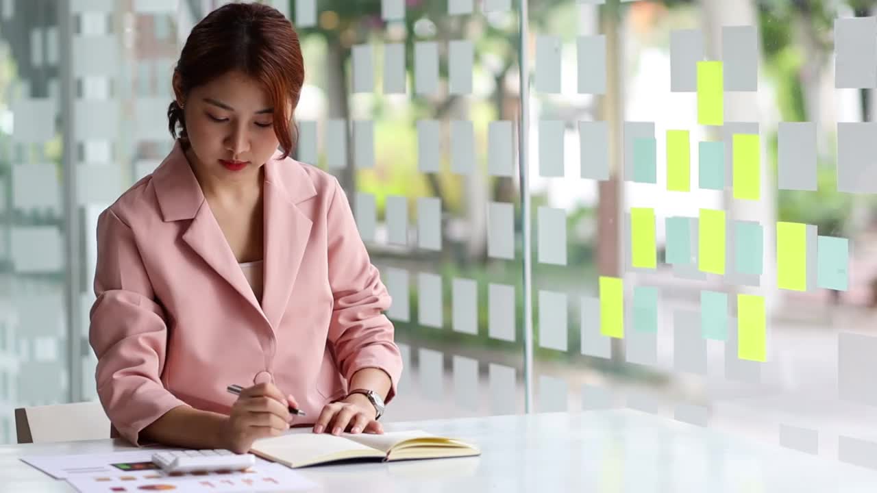 在金融行业工作的女商人正在用计算器计算预算，并在笔记本上写笔记。视频素材