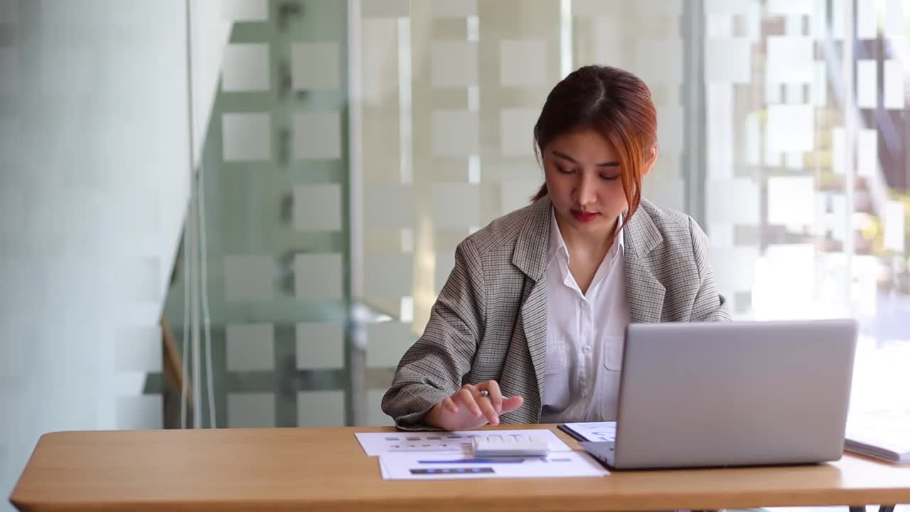 从事财务工作的女商人在银行办公室用计算器计算预算，同时在笔记本电脑上工作和审计文件，分析财务会计。视频素材