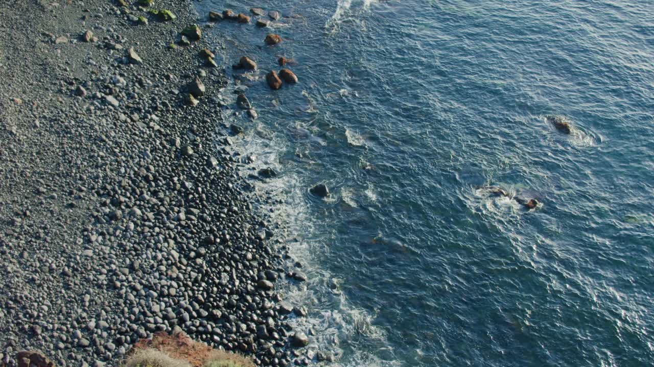 日落时，海浪冲击着火山流线型的石头。黑色的岩石海滩，平静的海洋，海浪形成泡沫。视频素材