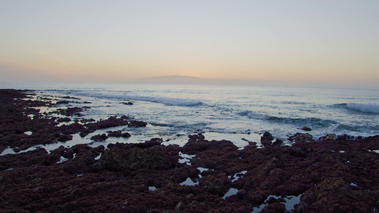 日落时海浪拍打在火山岩上。拉戈梅拉岛五彩缤纷的日落美景。低潮。藻类在岩石上。视频素材