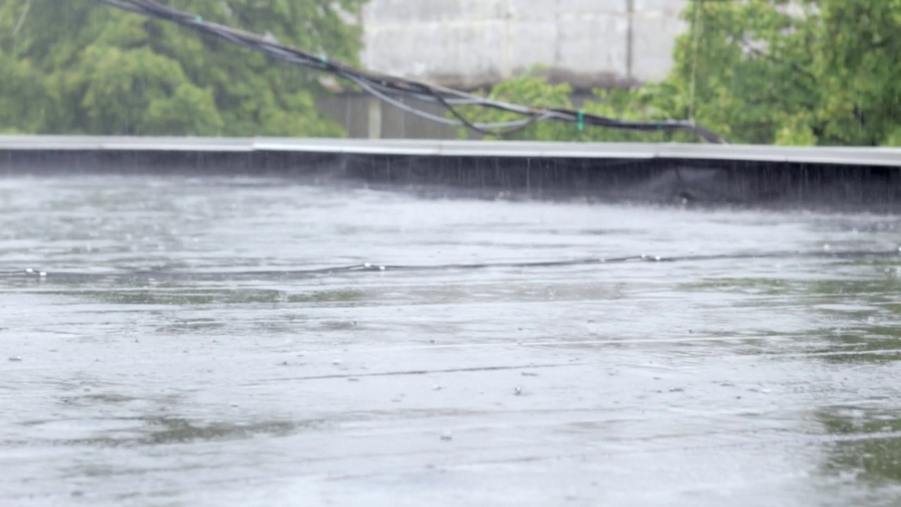 雨点敲打着屋顶，大雨滂沱。这座建筑的平屋顶覆盖着防水材料，可以防雨。橡胶、卷材屋面及防水材料。视频素材画面1