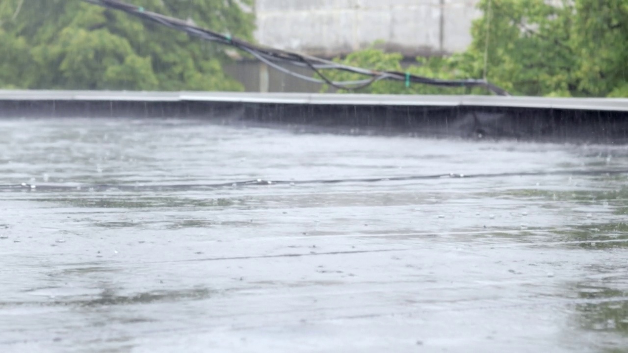 雨点敲打着屋顶，大雨滂沱。这座建筑的平屋顶覆盖着防水材料，可以防雨。橡胶、卷材屋面及防水材料。视频素材画面3