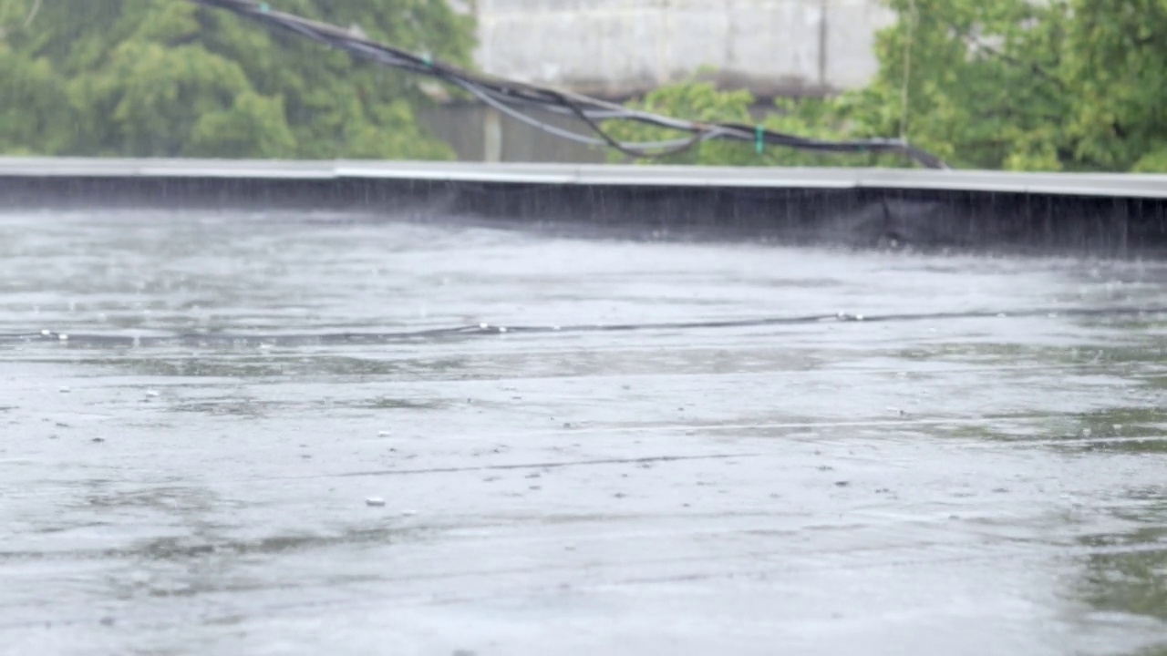 雨点敲打着屋顶，大雨滂沱。这座建筑的平屋顶覆盖着防水材料，可以防雨。橡胶、卷材屋面及防水材料。视频素材画面4