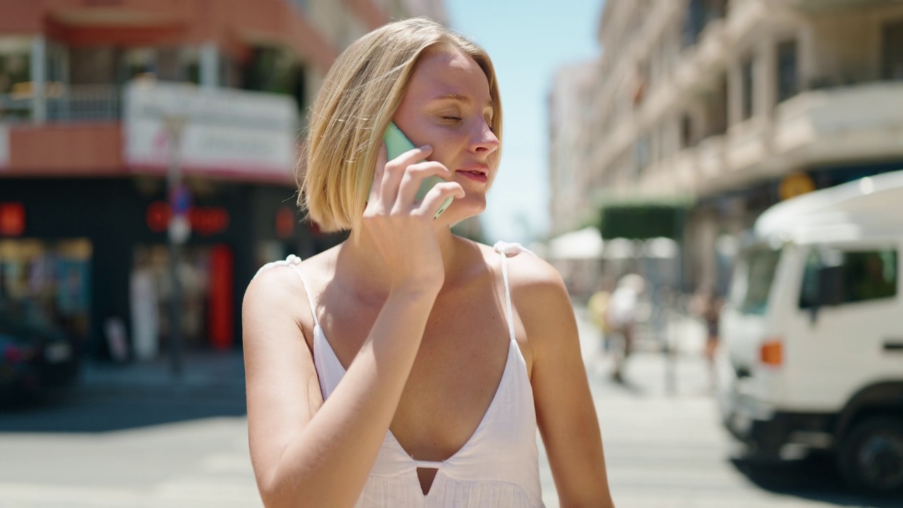 年轻的金发女子在街上用智能手机说话视频素材