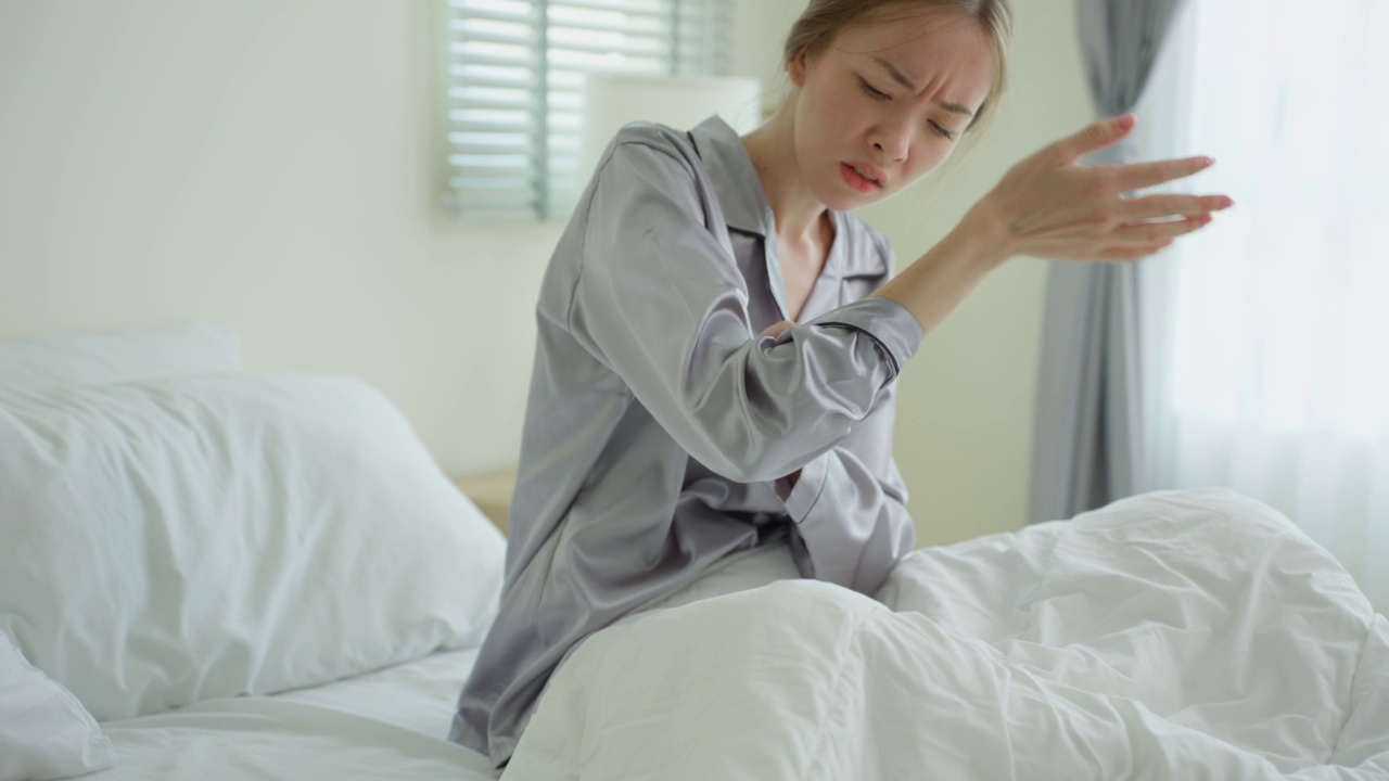 年轻的白人妇女早上醒来后搔手。美丽迷人的女孩躺在卧室的床上，忍受着昆虫叮咬引起的手臂皮肤过敏反应，皮炎。视频素材