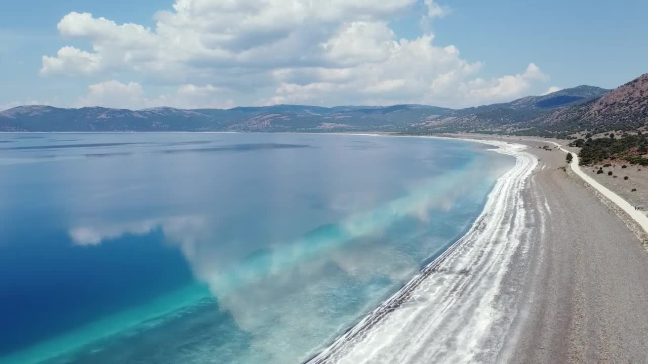 在群山的映衬下，四轴飞行器在蓝色的海水和白色的海滩之间飞行视频素材