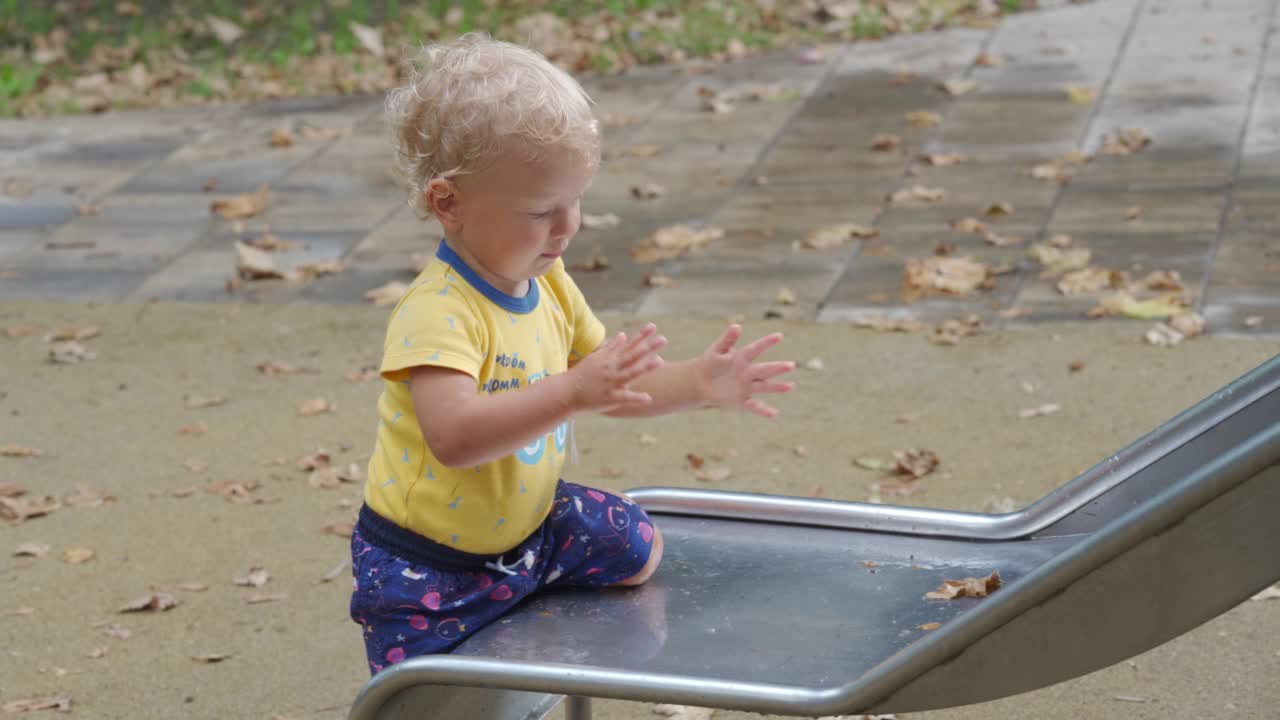 孩子在雨后潮湿的操场上玩耍，快乐的1.5岁幼童在一个雨天的夏天在公园里。儿童户外活动。视频素材