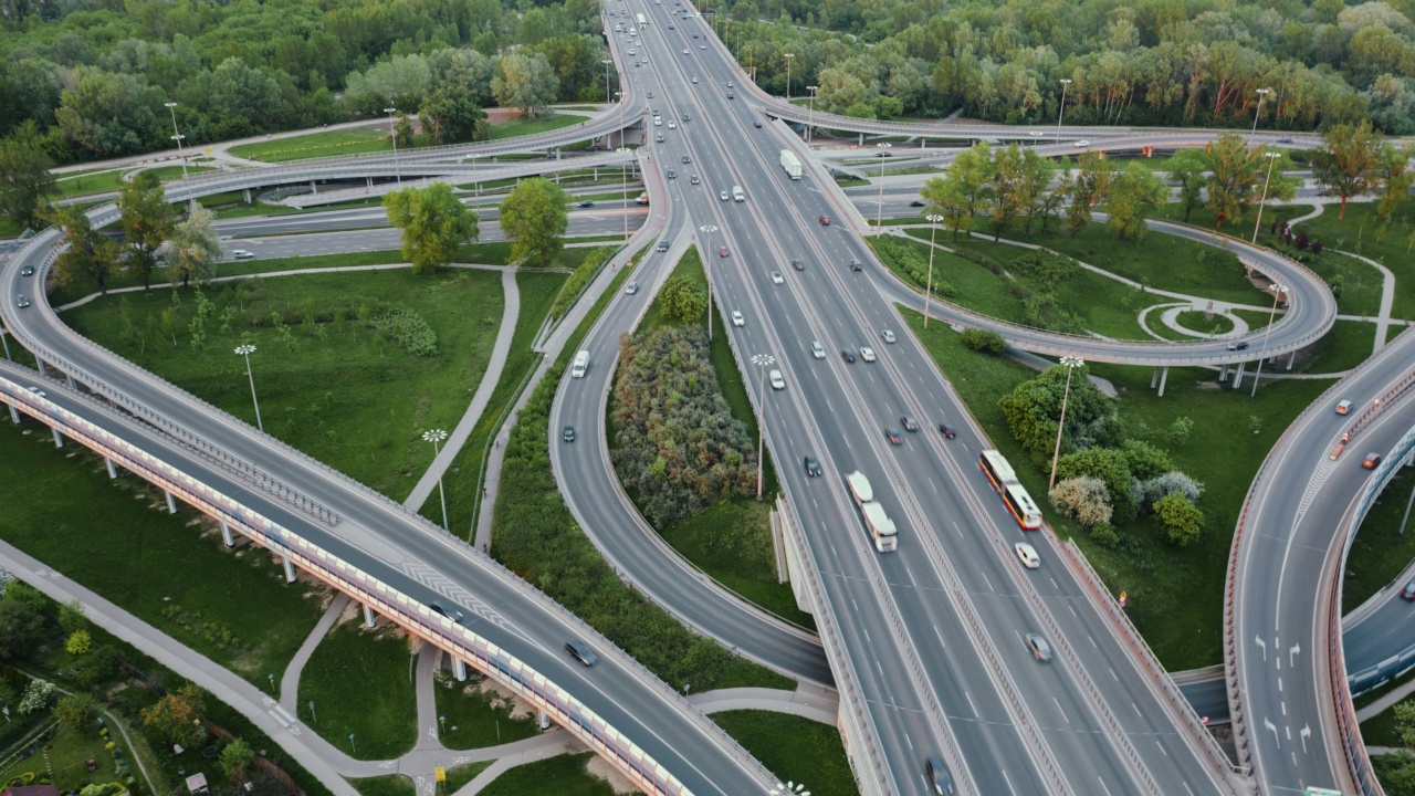 空中延时汽车交通绕行立交道路在傍晚，无人机拍摄的道路交叉口在城市。许多汽车行驶在繁忙的交叉公路。夏日，绿树绿草视频素材