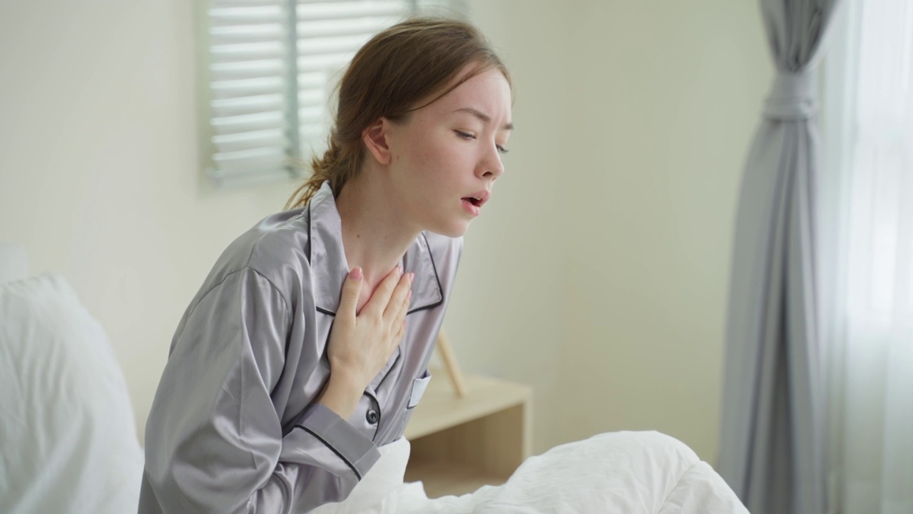 白种人漂亮的生病女孩穿着睡衣从卧室里起床。迷人的年轻女子在床上醒来后感觉不好，早上在家里咳嗽。健康care-lifestyles概念。视频素材