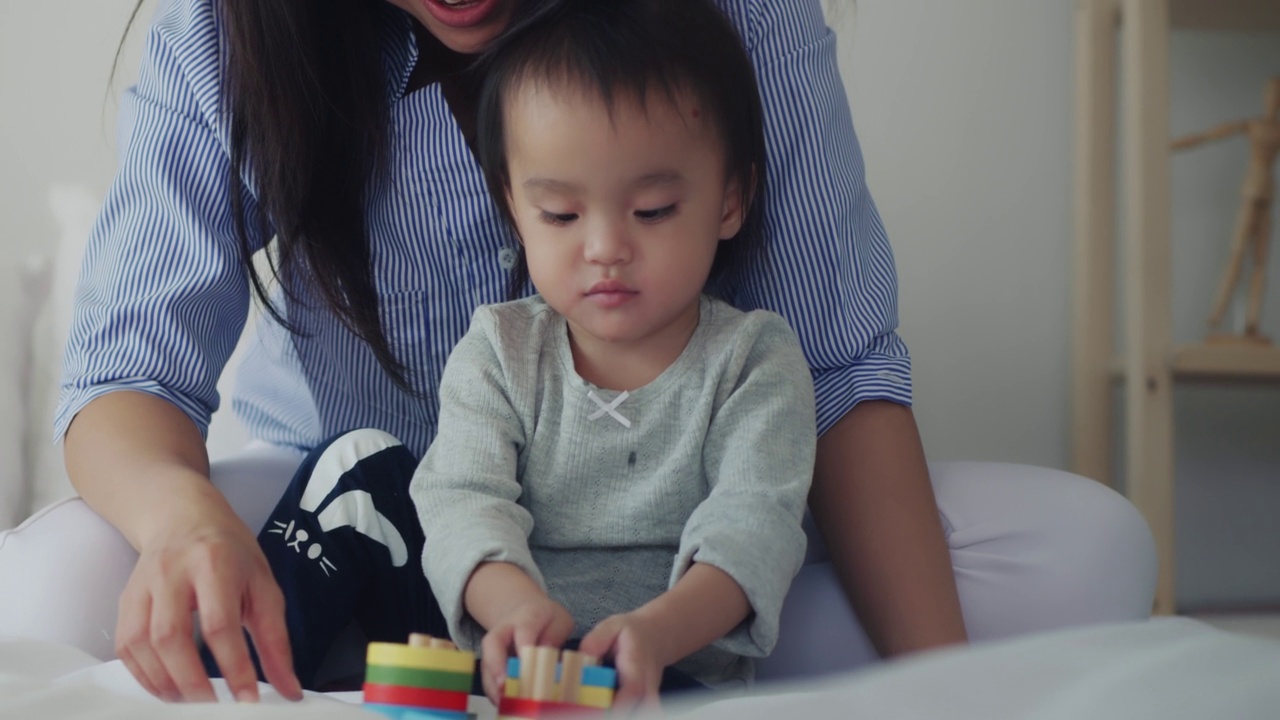 亚洲母亲和婴儿的孩子女孩学习玩彩色的木制玩具在床上视频素材