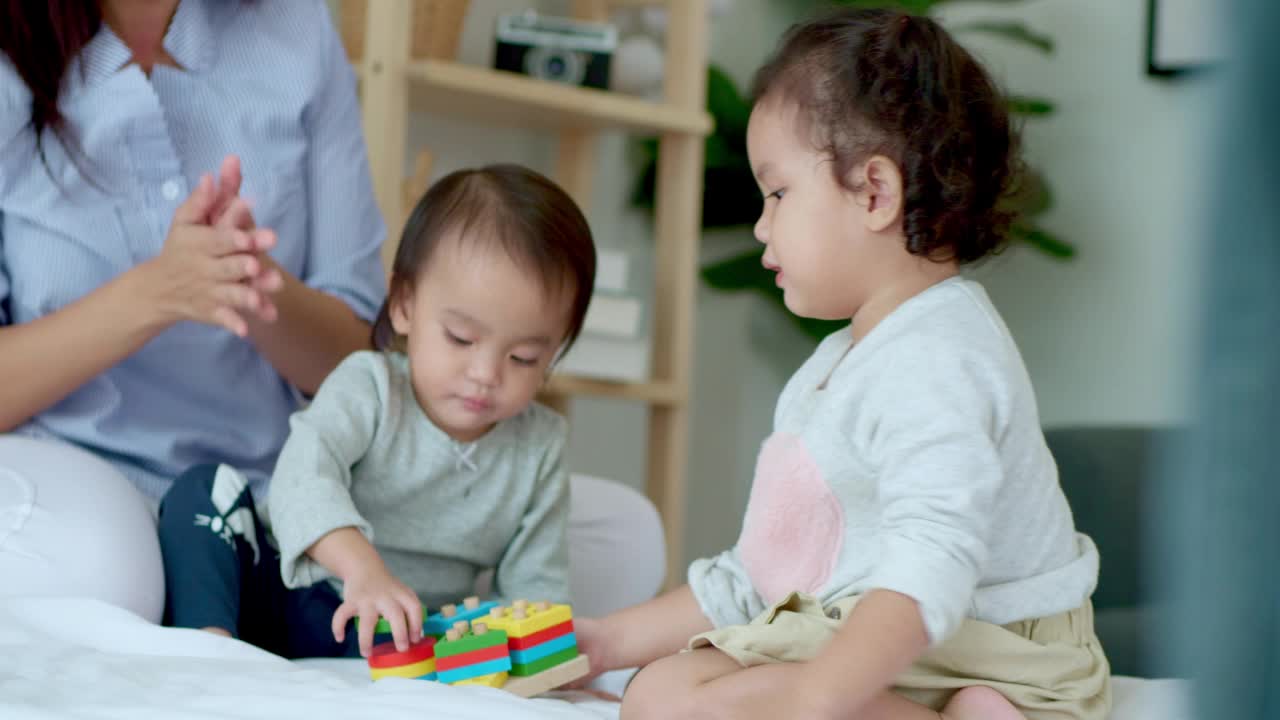 亚洲母亲和婴儿的孩子女孩学习玩彩色的木制玩具在床上视频素材