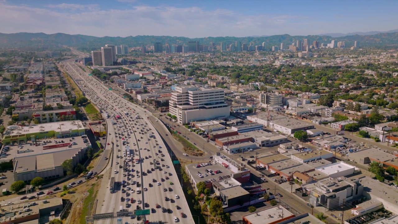 宽阔的多车道高速公路上满是汽车。飞越阳光普照的美国加利福尼亚州洛杉矶上空。朦胧的群山为背景。视频素材