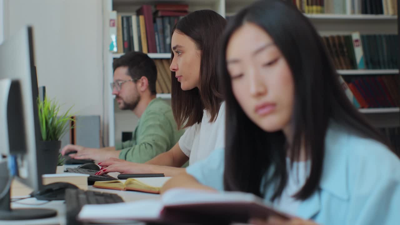 学生女生坐在桌前用电脑备考，在公共或大学图书馆用电脑写课文作业。视频素材