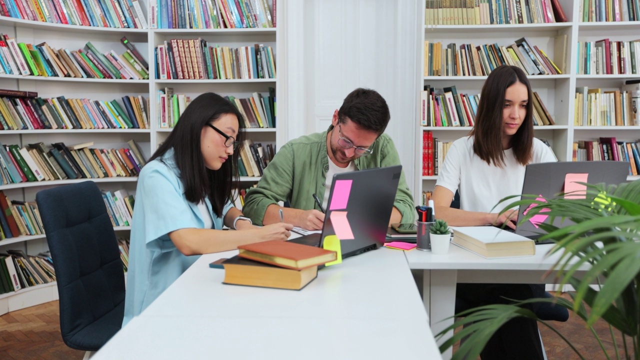 快乐的多民族大学生微笑着看着镜头，在现代化的大学图书馆摆姿势。教育，学习，现代科技理念。视频素材