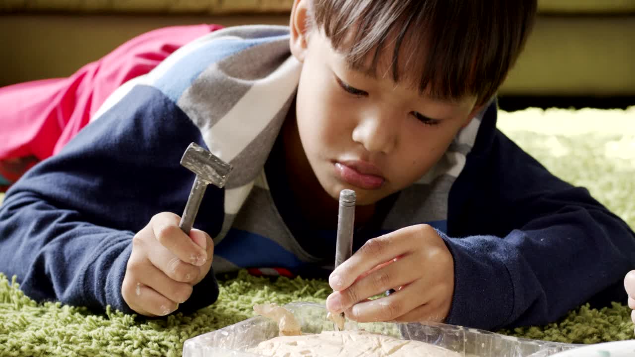 小男孩躺在地毯上，手里拿着锤子敲碎灰泥。视频素材