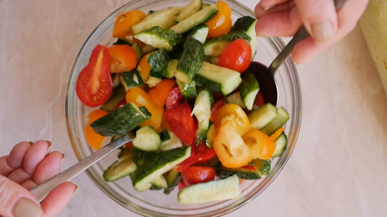 女子手拿两勺混合蔬菜沙拉与橄榄油素食餐。俯视图，慢动作视频素材