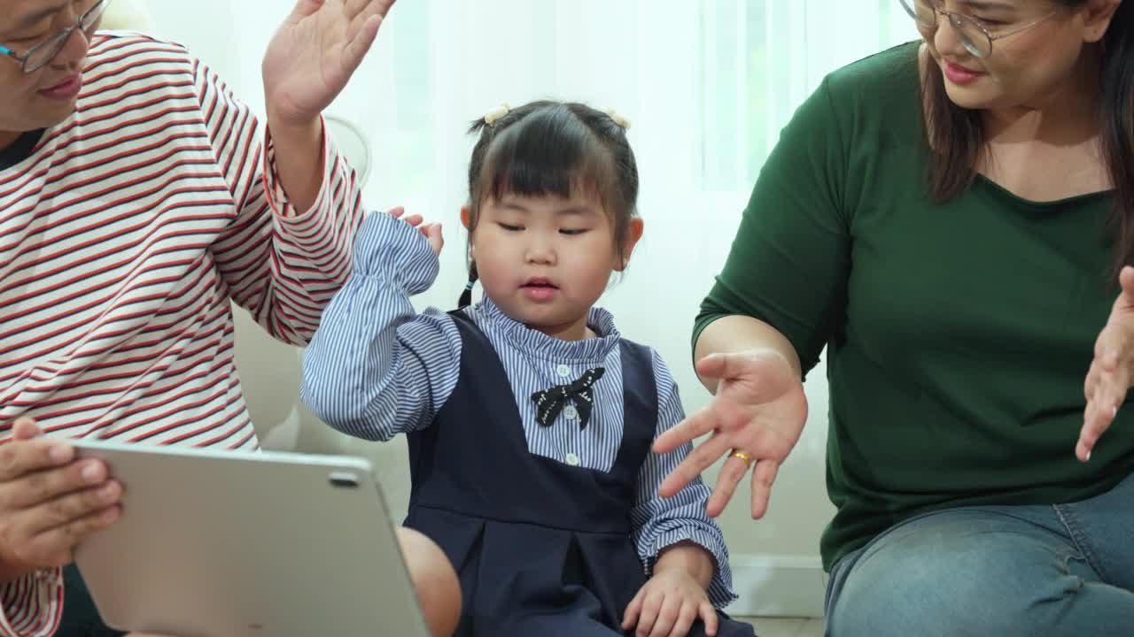 一对夫妇正在用平板电脑和现代科技促进他们可爱的小女儿的成长。视频素材