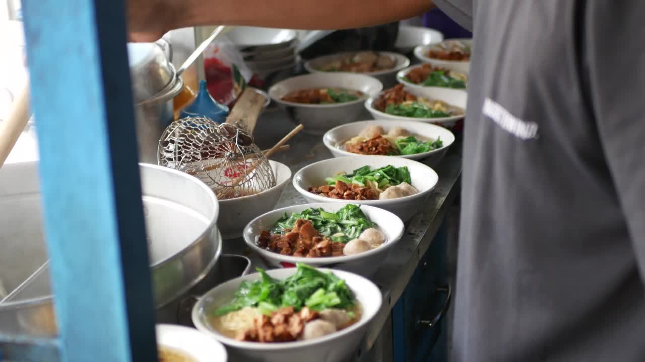 近距离观察一个penjuual mie ayam bakso或肉丸鸡肉面小贩谁正在为买家做鸡肉面。有选择性的重点。视频素材