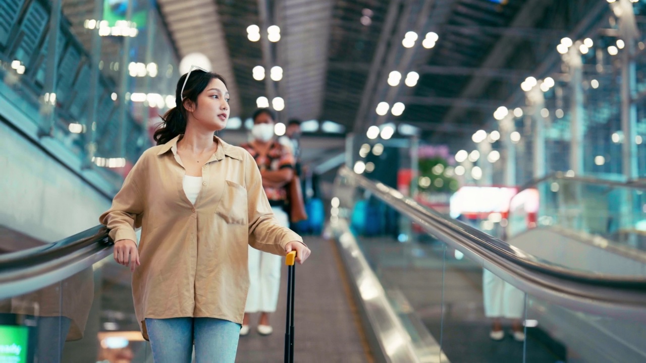 年轻的亚洲女乘客在机场候机楼或现代火车站。一名亚洲女性带着行李在自动扶梯上旅行视频素材