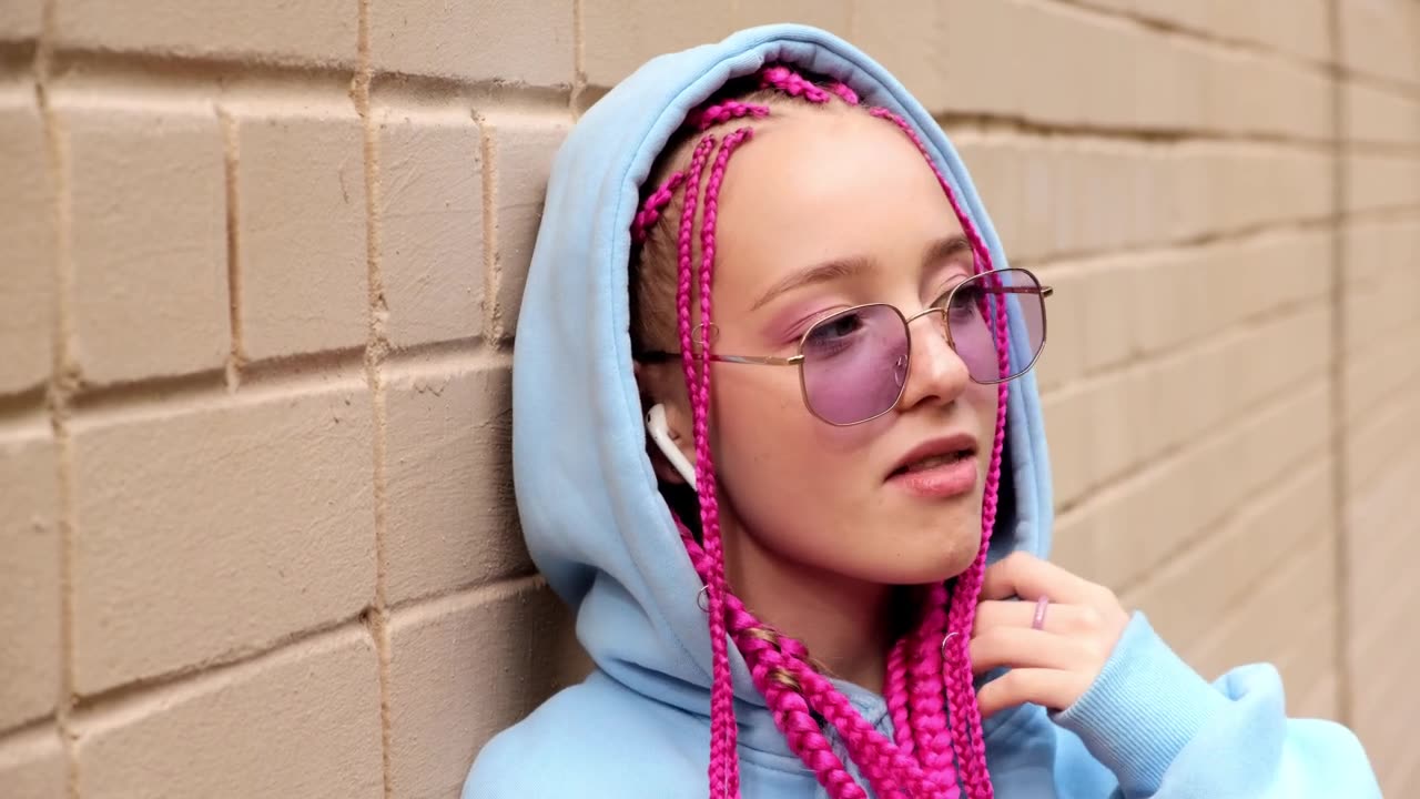 肖像的白人少女潮女孩粉红色的辫子对着粉红色的砖墙。Z一代的风格。视频素材画面1