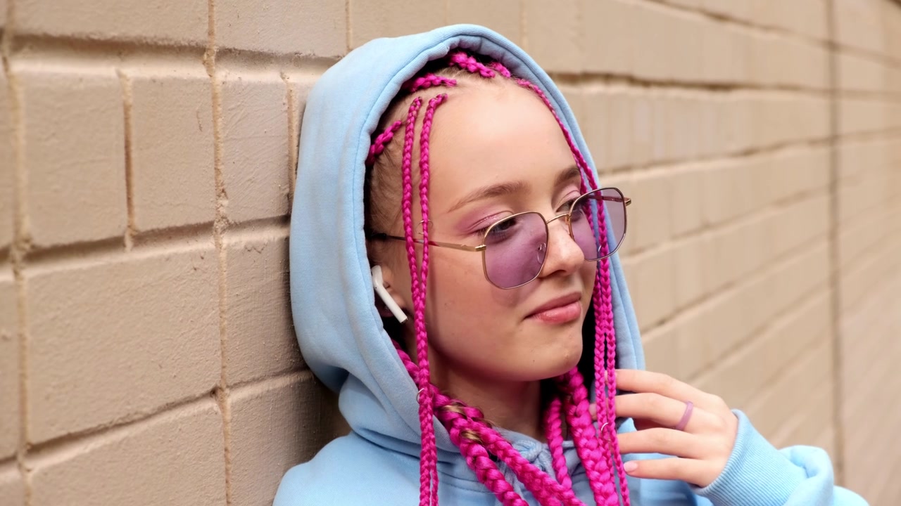 肖像的白人少女潮女孩粉红色的辫子对着粉红色的砖墙。Z一代的风格。视频素材画面2