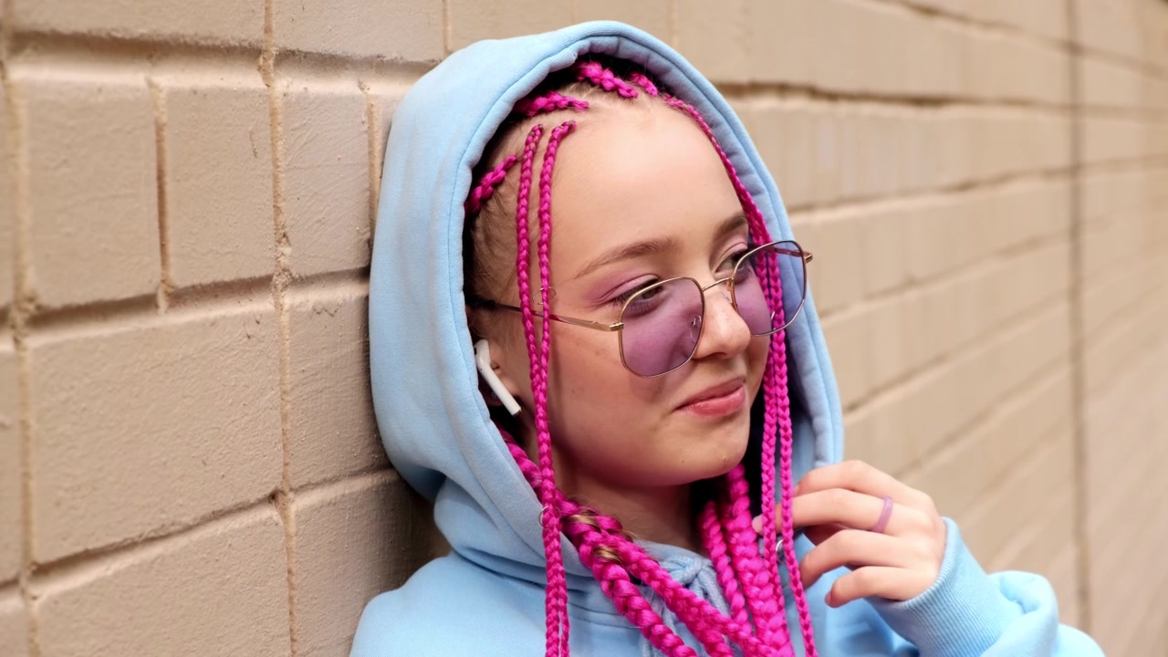 肖像的白人少女潮女孩粉红色的辫子对着粉红色的砖墙。Z一代的风格。视频素材画面3