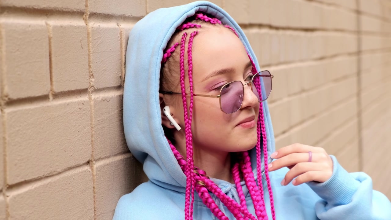 肖像的白人少女潮女孩粉红色的辫子对着粉红色的砖墙。Z一代的风格。视频素材画面4