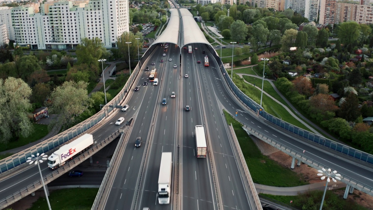 空中天桥交通堵塞的回旋立交道路在晚上，无人机拍摄的道路交叉口在现代城市。许多汽车在繁忙的十字公路上行驶。夏日里，绿树绿草视频素材