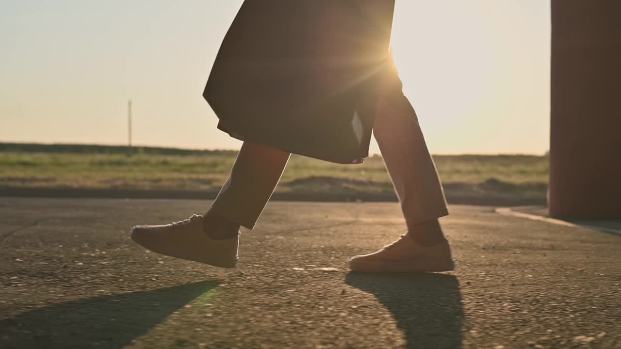 夕阳近景，年轻迷人的女孩穿着米色牛仔裤和白色运动鞋，提着纸袋买的东西穿过购物中心的街道停车场。电影镜头，慢动作视频素材