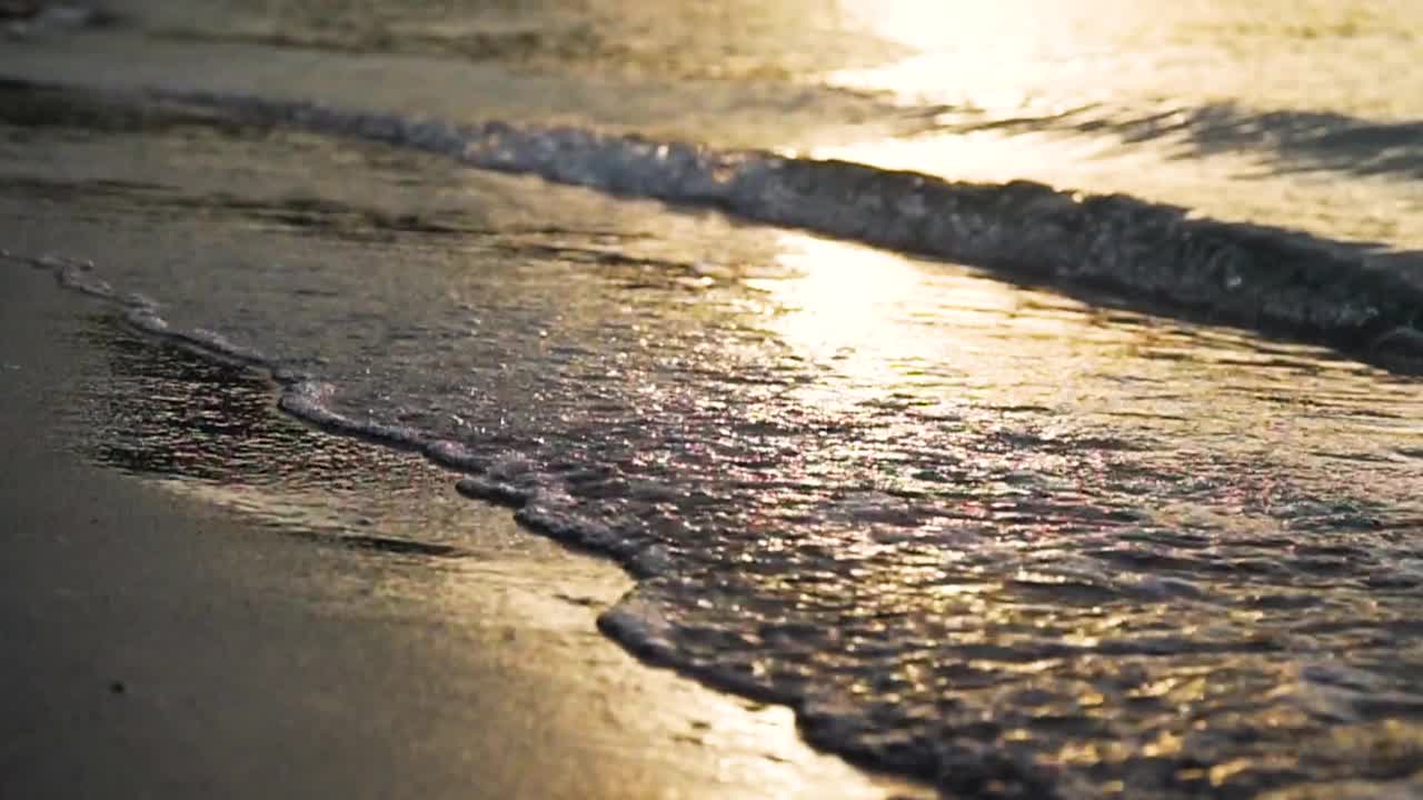 近景拍摄的海浪在日落时撞击沙滩的慢镜头视频素材