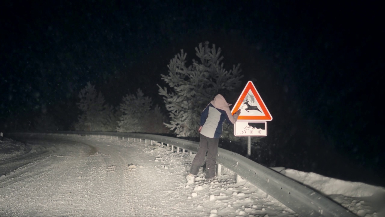 冬季夜晚，一名妇女正在清理警告牌，以防冬季降雪危险滑路视频素材