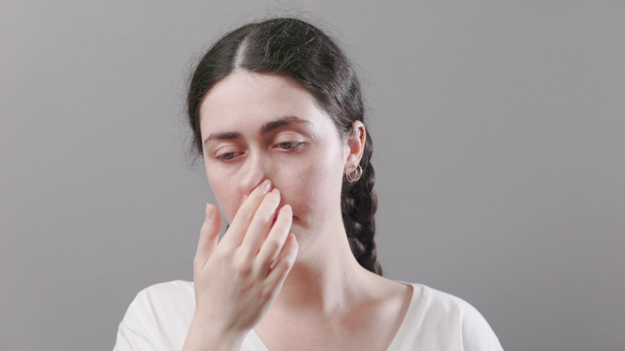 年轻生病的白人妇女触摸她的鼻子的肖像。治疗流鼻涕和病毒感染。灰色的背景。过敏和流感的概念视频素材