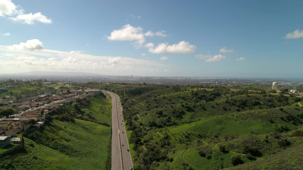 空中拍摄的汽车在绿色的山脉之间的道路上移动，无人机在晴朗的日子在云层下向前飞行-洛杉矶，加利福尼亚州视频素材