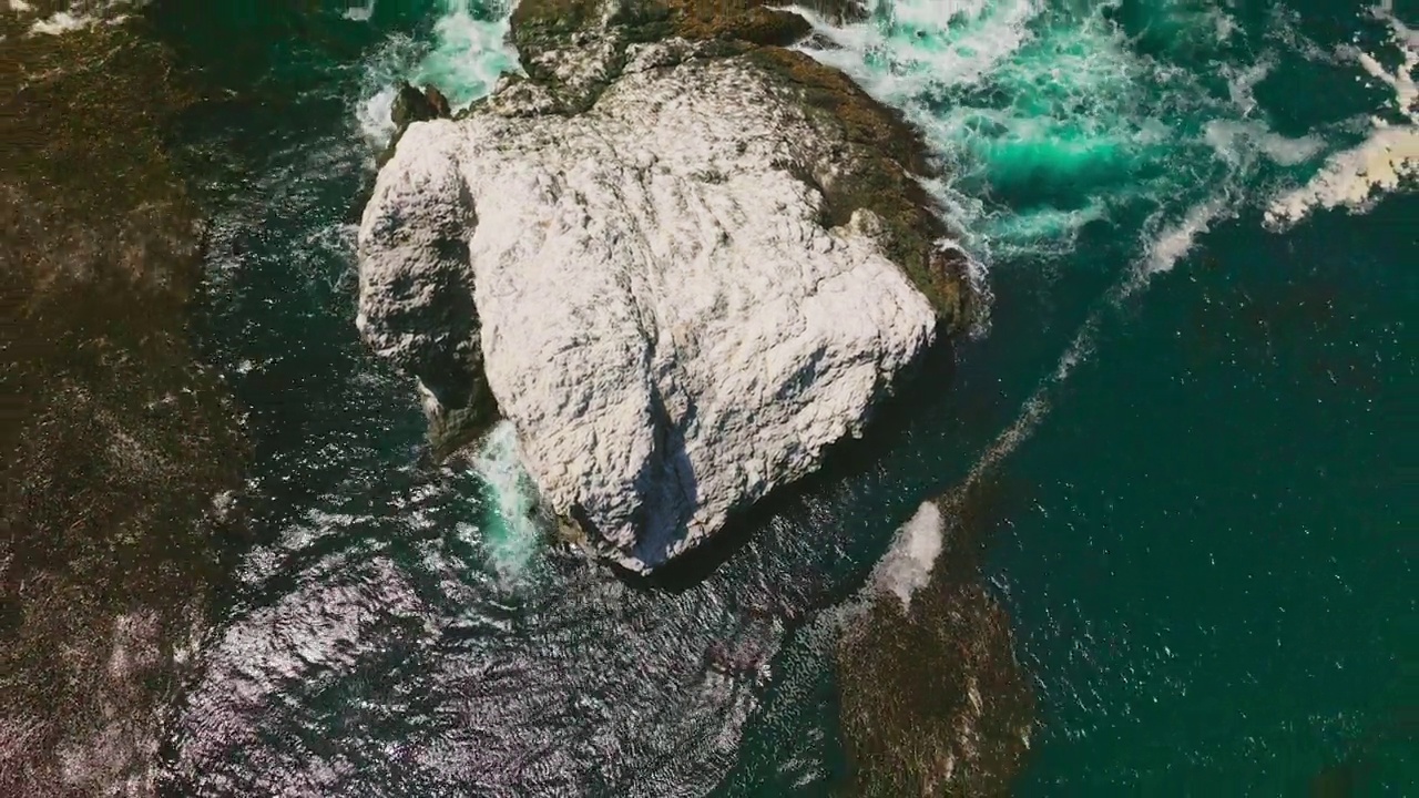 在加利福尼亚海岸，覆盖着盐的岩石从太平洋的海蓝色海水中露出来。藻类漂浮在水面上。鸟瞰图。视频素材