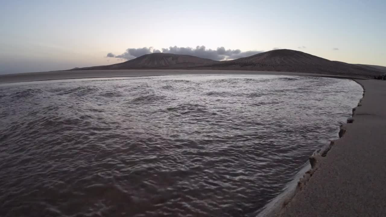 退潮时，潮水从泻湖流回大海，背景是火山视频素材