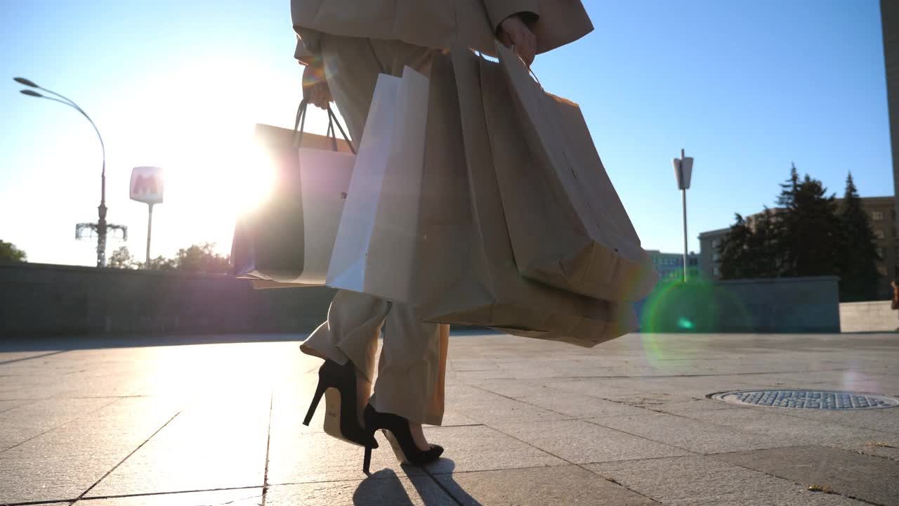 小女孩背着纸包走在城市的街道上。美丽的女人拿着购物袋在城市广场购物后。销售和折扣的概念。近景慢镜头特写视频素材