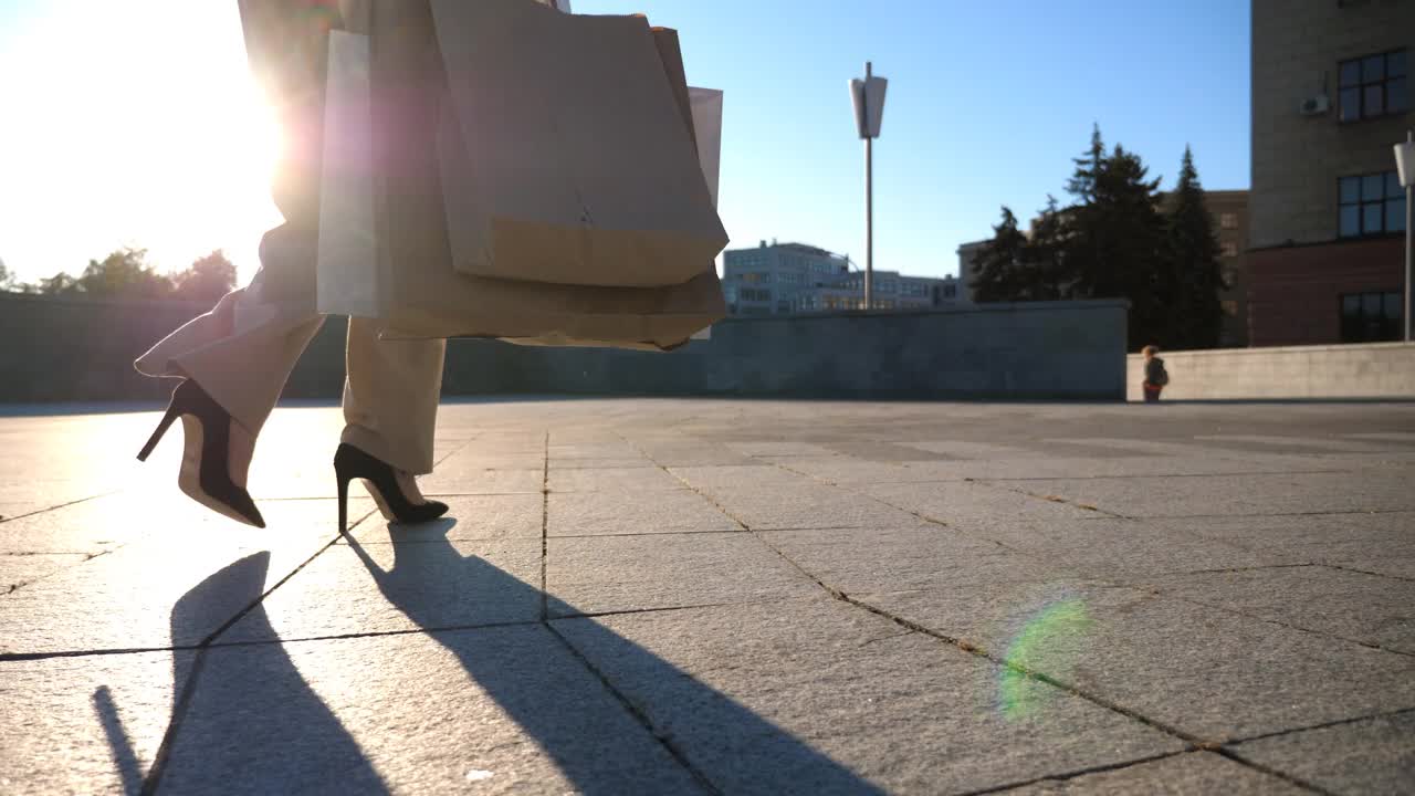 小女孩背着纸包走在城市的街道上。美丽的女人拿着购物袋在城市广场购物后。销售和折扣的概念。近景慢镜头特写视频素材