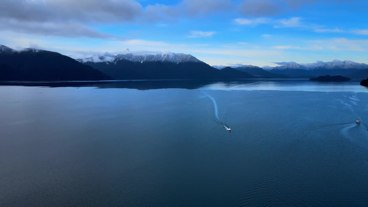 智利南部托多斯·洛斯桑托斯湖的鸟瞰图。背景是云和雪山和平提阿瓜多火山。船留下了痕迹。视频素材