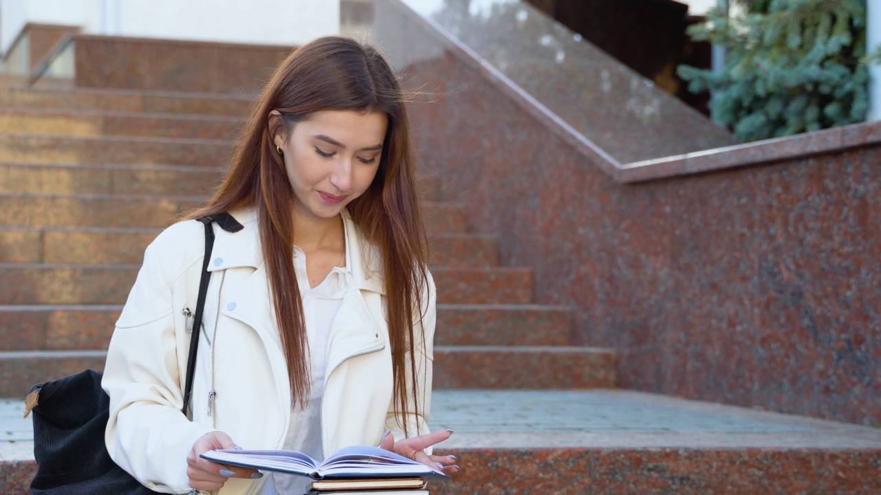 一个年轻的女学生坐在大学校园的楼梯上看书视频素材