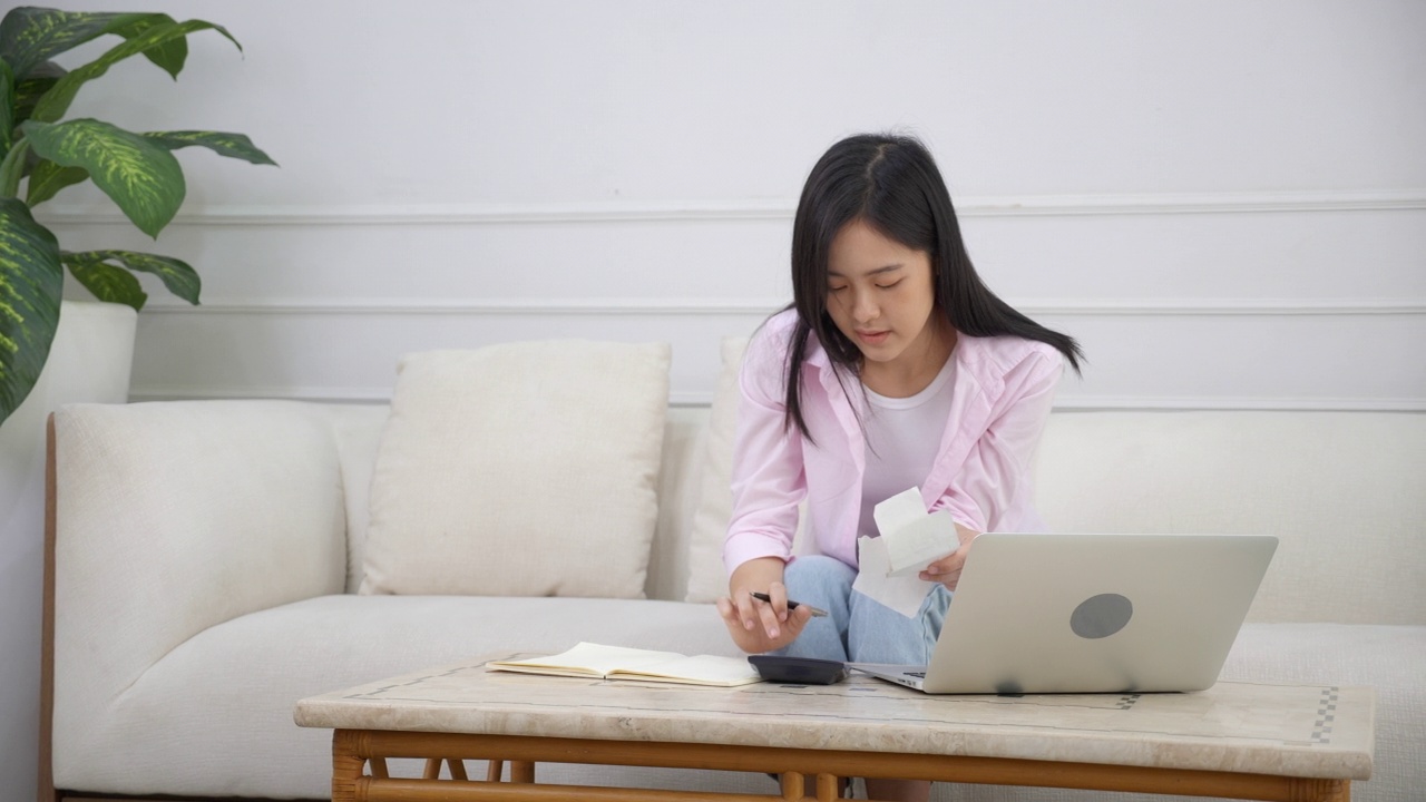 年轻的亚洲妇女计算开支家庭财务和沮丧在家里，女孩核对账单有压力和担心，债务和税收，表情和情绪疲劳，经营理念。视频素材