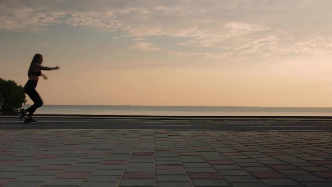 年轻女子在做侧空翻。女孩在日出时对着大海做杂技活动。健身生活方式慢动作。视频素材