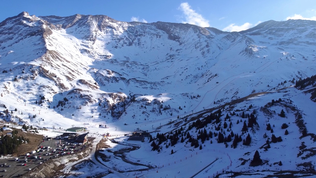 无人机在塞勒滑雪场的停车场上空飞行，滑雪场位于雪山之间视频素材