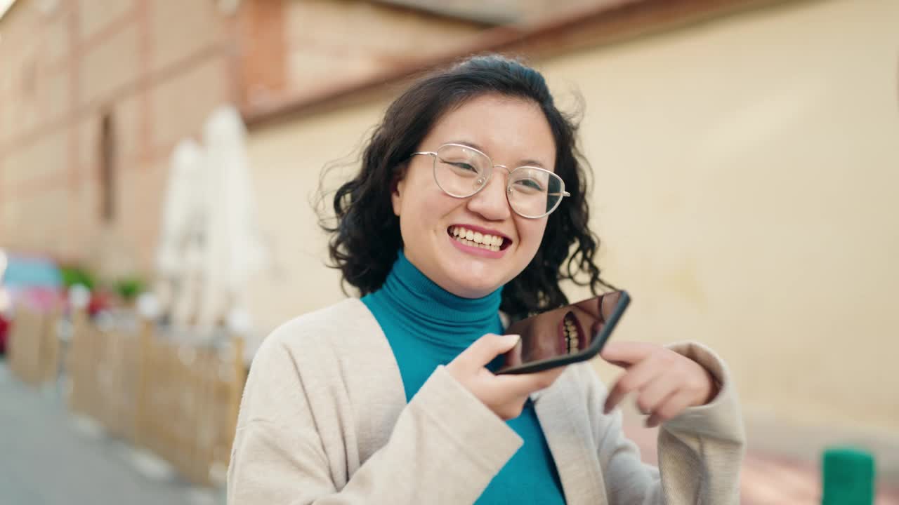 年轻的中国女子微笑着自信地在街上用智能手机聊天视频素材