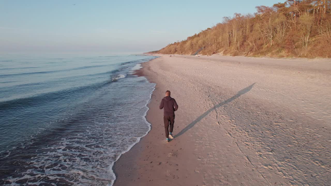 一个跑步者，在日落时分，他沿着海滩沿着海浪奔跑。视频素材