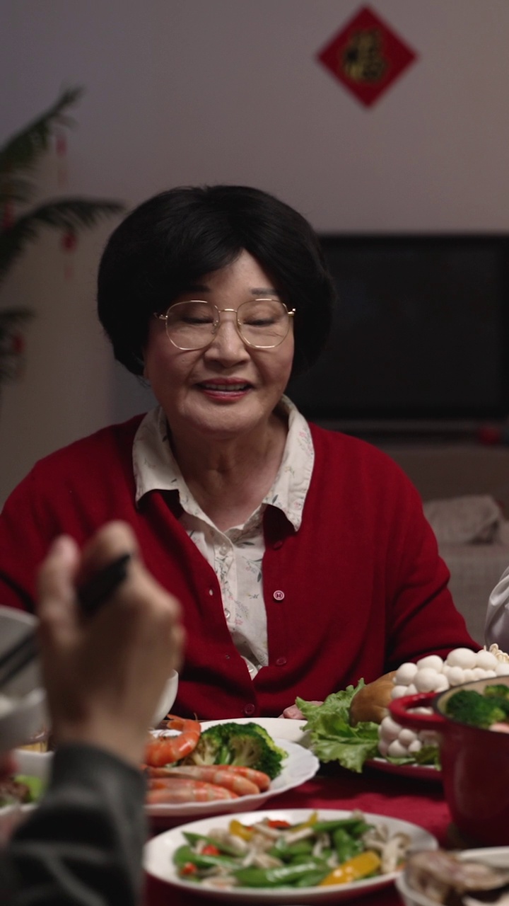 竖屏:中国农历除夕夜，亚裔大妈在吃大餐时，用筷子给儿媳喂饭。翻译:幸运视频素材画面2