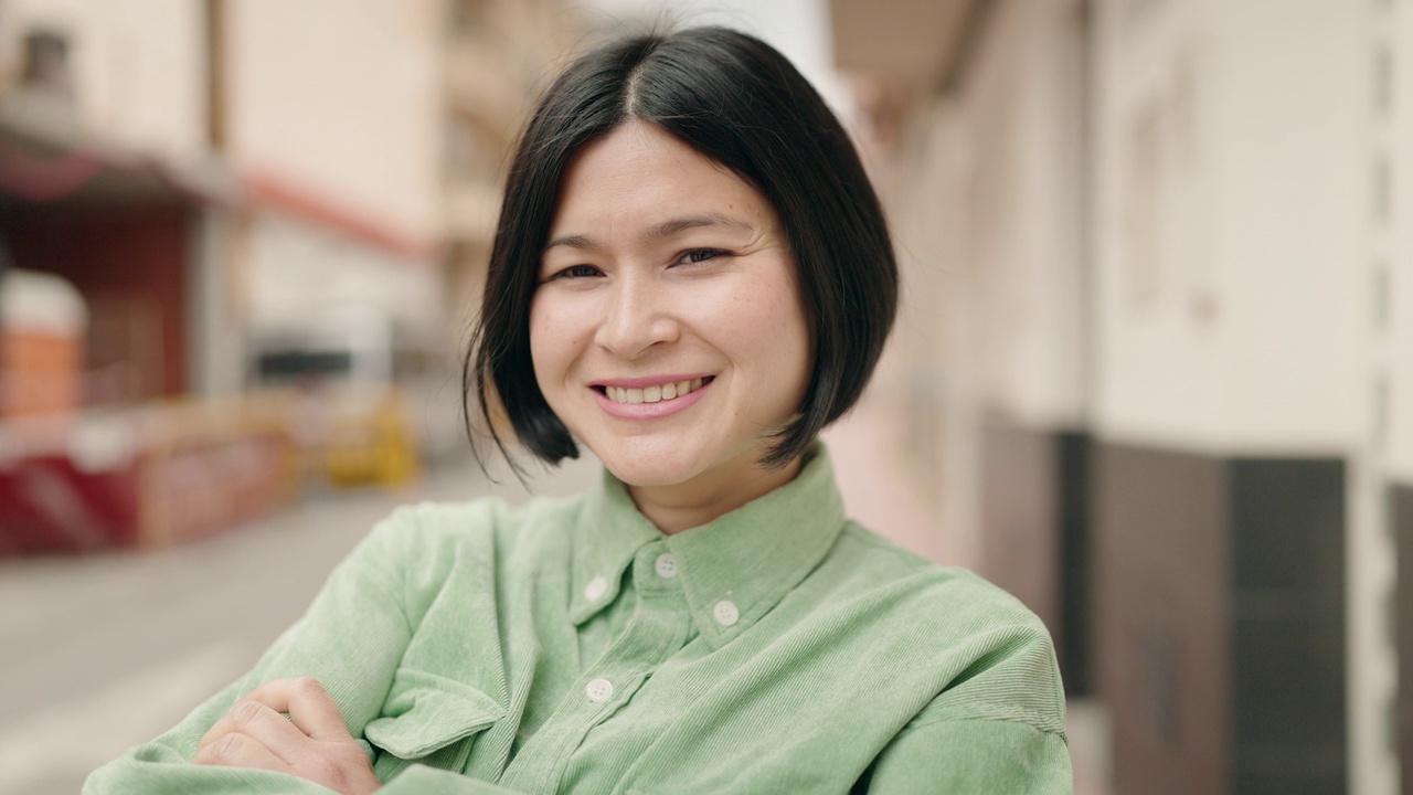 年轻的中国女子微笑着，自信地站在街上，双手交叉视频素材